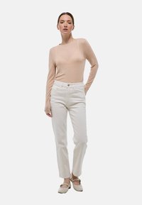 Un haut beige clair à manches longues associé à un jean droit blanc et des chaussures claires. Le tissu du haut semble transparent et lisse.