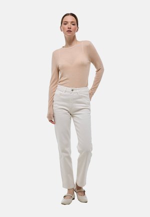 Un haut beige clair à manches longues associé à un jean droit blanc et des chaussures claires. Le tissu du haut semble transparent et lisse.