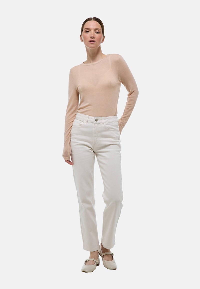 Un haut beige clair à manches longues associé à un jean droit blanc et des chaussures claires. Le tissu du haut semble transparent et lisse.