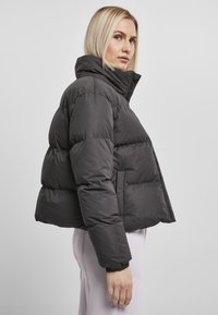 Melnā īsā puffer jaka ar augstu apkakli, kvadrātveida dizainu un elastīgām piedurknēm. Gluda tekstūra ar rāvējslēdzēju un sānu kabatām.