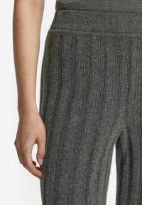 Grå ribbet stofleggings med lodrette striber, en bredalastisk talje og en blød tekstur. Nærbillede af stoffet og en hånd.