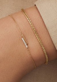 Bracelet en ton or avec un design de chaîne torsadée et une chaîne fine avec une barre en ton argent et des accents texturés.