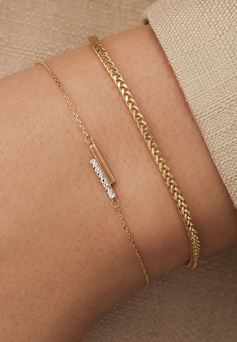 Bracelet en ton or avec un design de chaîne torsadée et une chaîne fine avec une barre en ton argent et des accents texturés.