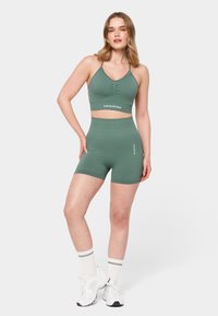 Roheline spordibralette ja kõrge vöökoht, mis on valmistatud siledast kangast ja omab keha lähedast disaini. Omab kurrutuste detaile ja logo aktsente.