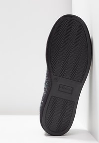 Svart mockasole med texturerat zigzag-mönster och logotyp. Mjuk ovandel med färgglada fläckar som skapar en blandad effekt.