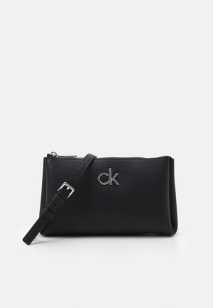 Pulsera de cuero negro con logo "ck" en plata, correa ajustable y cierre de cremallera superior sobre un fondo claro y liso.