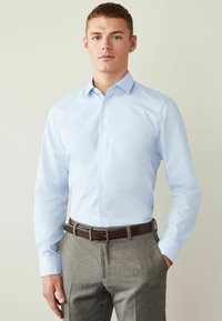 Himmelblaues Hemd mit langen Ärmeln, aus Baumwollstoff, kombiniert mit grauen Hosen und einem braunen Leder Gürtel. Einfaches Kragen Design.