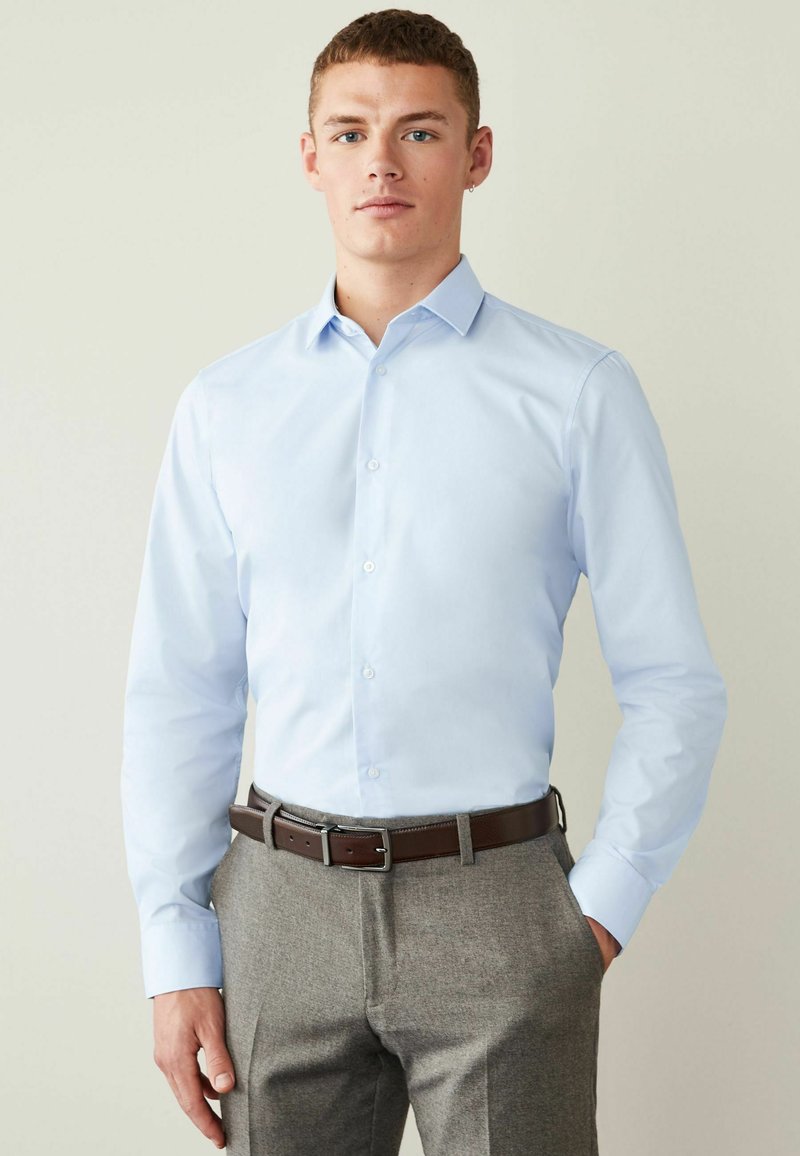Himmelblaues Hemd mit langen Ärmeln, aus Baumwollstoff, kombiniert mit grauen Hosen und einem braunen Leder Gürtel. Einfaches Kragen Design.