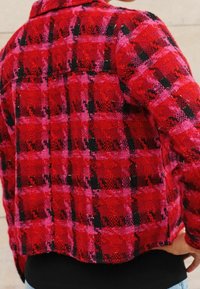 Punainen ja vaaleanpunainen ruudullinen takki teksturoidusta kankaasta; ominaisuuksina mustat korostukset ja kauluksellinen malli näkyvine ompelusaumoineen.