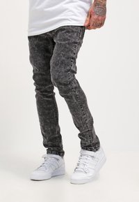 Slim-fit gray acid-washed jeans with a textured finish, paired with white sneakers. Visible distressed detailing along the legs.