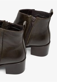 Donkergroene leren enkellaarzen met een afgeronde neus, lage blokhak en ritsen aan de zijkant. Voorzien van een gladde afwerking en subtiele stikdetails.