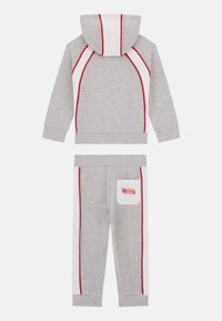 Grauer Kapuzenpullover und passende Hose mit roten und weißen Akzenten. Aus weichem Stoff, mit gerippten Bündchen und einer Seitentasche an der Hose.