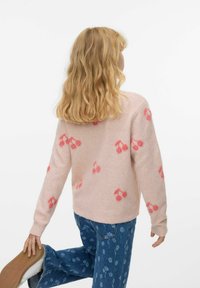 Różowy sweter w wzór wiśni, miękka faktura, długie rękawy i klasyczny krój. Noszony z dżinsowymi spodniami w kwiatowy nadruk.