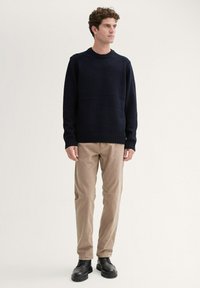 Pull en maille bleu marine avec un col rond côtelé, associé à un pantalon en velours côtelé beige et des bottes noir à lacets, présenté sur un fond neutre.