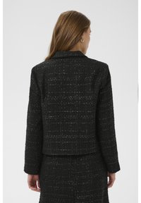 Juodas tweedo švarkas su tekstūruota audinio faktūra, trumpintu dizainu, nertais atlapais ir ilgomis rankovėmis, rodantis subtilų blizgesį ir austus detalius elementus.