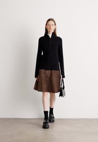 Maglione nero con zip abbinato a una gonna svasata marrone con motivo a spina di pesce. Scarpe con plateau nere e una borsa a tracolla piccola.