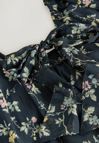 Blommig blus i marinblått tyg med ljusrosa och gula blommor. Inkluderar en knytdetalj vid halsen och ett elastiskt midjeband.