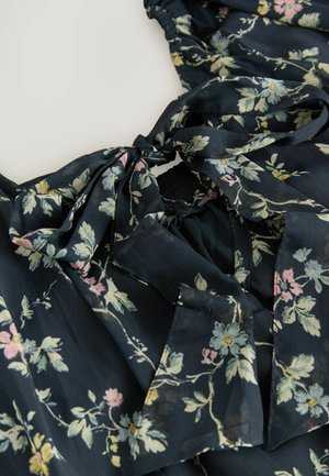 Blusa floreale in tessuto blu navy con fiori rosa chiaro e gialli. Include un dettaglio con fiocco sul collo e una vita elasticizzata.