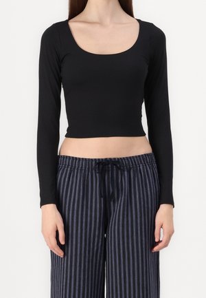 Kvinde iført en sort langærmet cropped top og højtaljede løse bukser med sorte og grå lodrette striber.