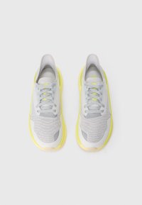 Sneakers grigi e bianchi con suole e lacci giallo neon, visti dall'alto su uno sfondo bianco.