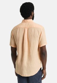 Kurzarmhemd aus leichtem Pfirsichleinen, mit einem klassischen Kragen, Rückenschlitz und abgerundetem Saum. Strukturiertes Gewebe und legere Passform.