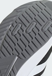 Suola esterna in gomma grigia con motivo scolpito, caratterizzata da profonde scanalature e sezioni rialzate per una maggiore aderenza. Accento bianco sul lato.
