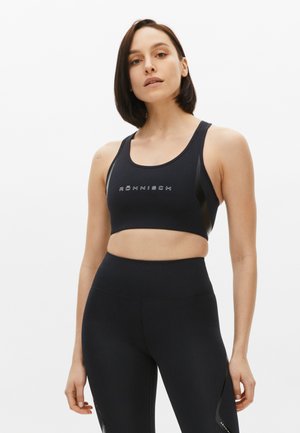 Top sportivo nero con logo, caratterizzato da un scollatura a U e spalline a canottiera. Abbinato a leggings neri a vita alta con discreti dettagli laterali.