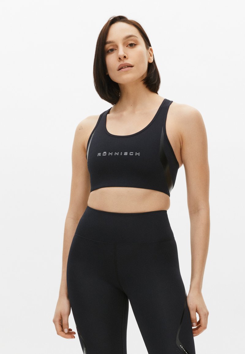 Sujetador deportivo negro con logo, con escote redondeado y tirantes tipo tank. Combinado con leggings negros de cintura alta con sutiles acentos laterales.