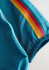 Zöld sport mez bordázott textúrával, piros, narancssárga és sárga merész csíkokkal a vállvarrás mentén.