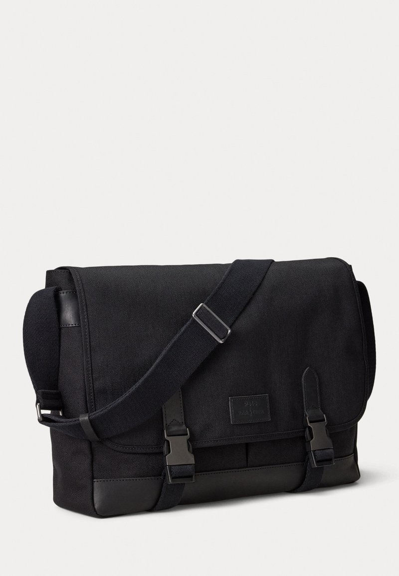 Borsa messenger nera in materiale canvas, con tracolla regolabile, chiusura a patta e accenti in pelle a contrasto. Presenta dettagli con fibbie sul davanti.