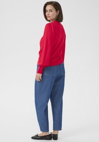 Red long-sleeve sweater with gathered shoulders, paired with loose blue denim jeans. Black flat shoes complete the outfit.