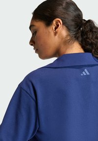 Granatowy sweatshirt o subtelnej fakturze, z kołnierzem i małym jasnoniebieskim logo Adidas z tyłu.