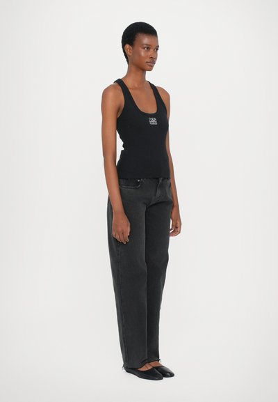 Black tank top with a square neckline and a small logo, paired with high-waisted dark gray wide-leg jeans and black flat shoes.