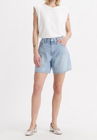 Light blue denim shorts with a high waist, relaxed fit, and rolled hem. Paired with a white sleeveless top and silver ballet flats.