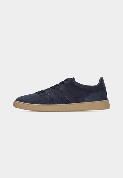 Zapatilla deportiva de ante azul marino para hombre con suela de goma marrón claro, cordones negros y un detalle en relieve de la letra "H" en el lateral, mostrada de perfil.