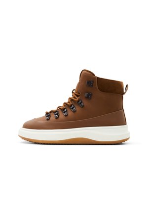 Botas de senderismo altas marrones hechas de cuero y ante, con ganchos de metal para los cordones, una media suela blanca y una suela exterior de goma.