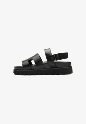 Black sandal featuring multiple straps, a cushioned sole, and a chunky black outsole with a zigzag pattern for traction.
