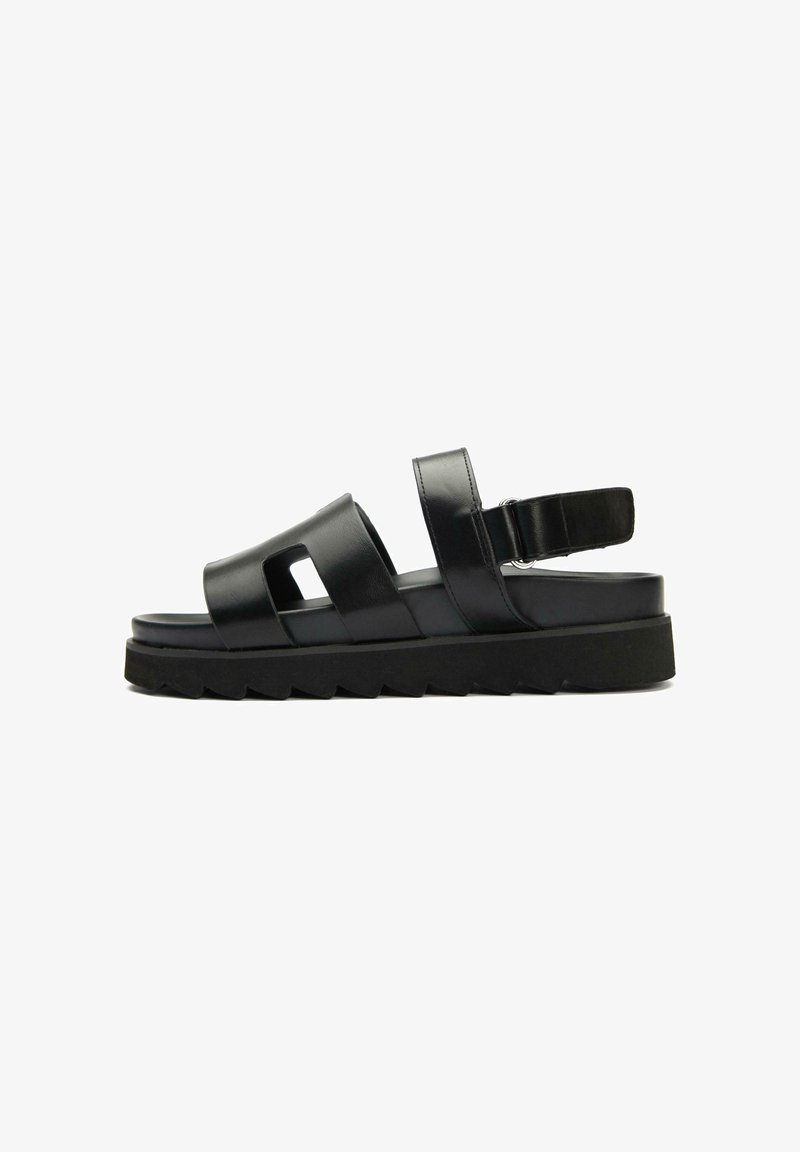 Black sandal featuring multiple straps, a cushioned sole, and a chunky black outsole with a zigzag pattern for traction.