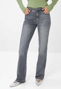 Jeans in denim grigio con un taglio dritto, dotati di tasche frontali e vita aderente, abbinati a scarpe argentate con punta a punta.