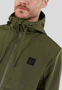 Veste à capuche vert olive avec fermeture éclair, cordons de serrage ajustables et un patch logo noir sur la poitrine. Texture de tissu lisse.