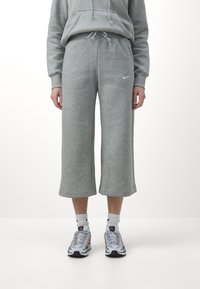 Grå sweatpants i mjuktyg med lös passform, kortare längd, elastisk midja och en liten vit logotyp på vänster sida.