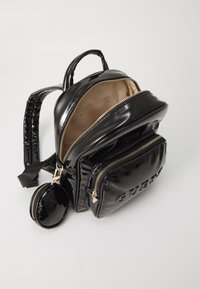Sac à dos en cuir verni noir avec une finition brillante, équipé de quincaillerie en or, de plusieurs compartiments zippés et d'une petite pochette ronde attachée.