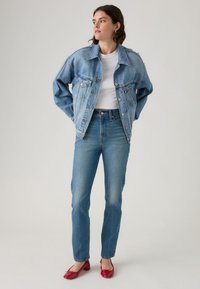 Ανοιχτό μπλε τζιν μπουφάν με χαλαρή εφαρμογή, λευκό πουκάμισο, ανοιχτό μπλε τζιν και κόκκινα παπούτσια από πατενέ δέρμα. Απλός σχεδιασμός με ελάχιστες λεπτομέρειες.