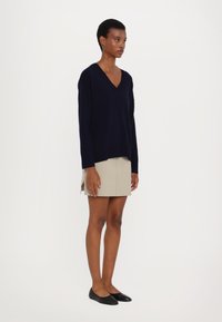 Pulover bleumarin cu decolteu în V, mâneci lungi, fabricat dintr-un material moale, asortat cu o fustă bej deschis. Pantofi negri, cu talpă joasă, design simplu, cu accente minime.