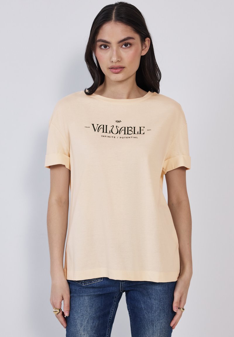 Camiseta de manga corta color durazno hecha de tela suave, con un estampado en negro que dice "TU VALIOSO CAMINO INFINITO / POTENCIAL."