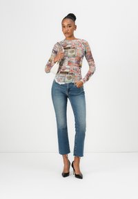 Long-sleeve top with a colorful retro gas station print, paired with fitted blue jeans and black high heels, held with a white handbag.