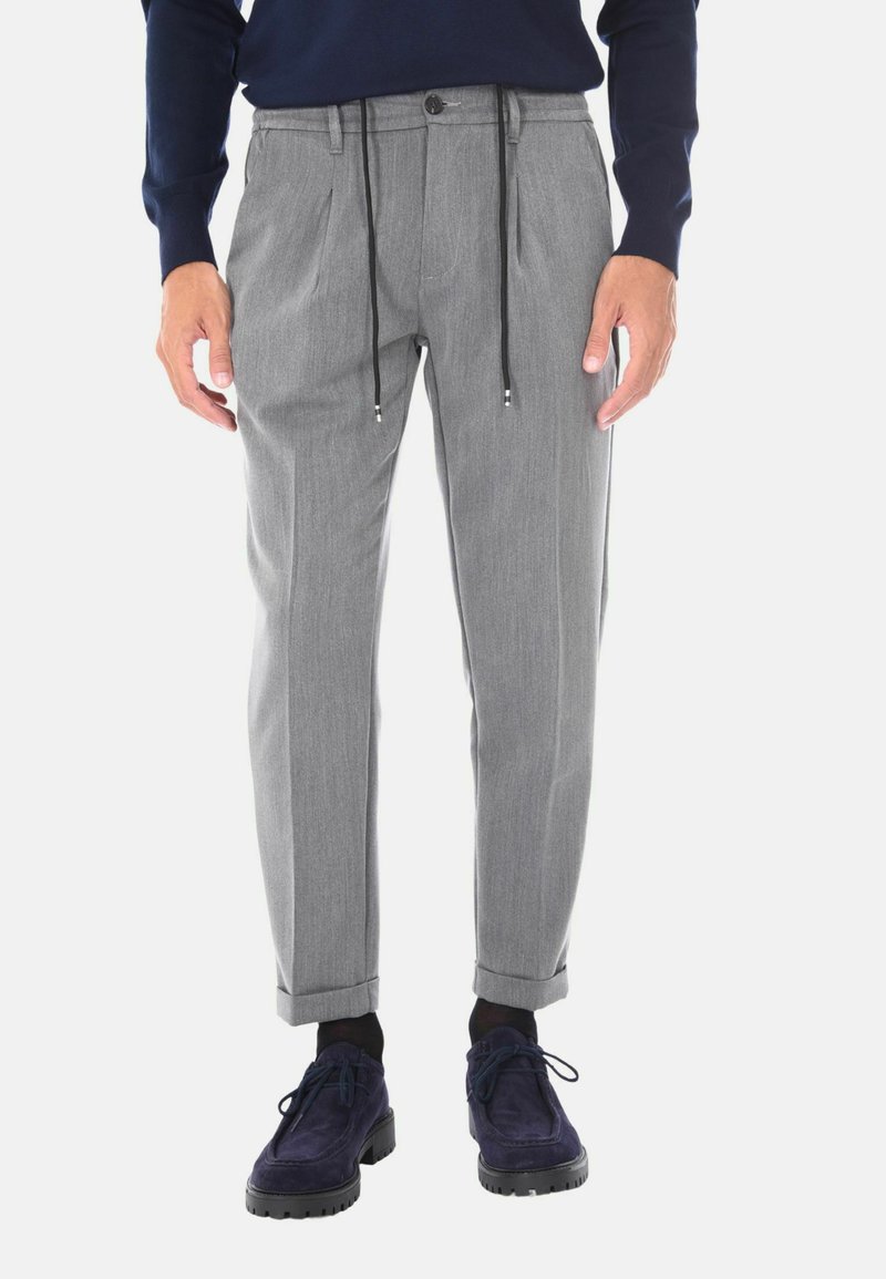 Pantaloni grigi a sigaretta con vita regolabile e tasche laterali. Tessuto morbido, leggero, con risvolti, abbinati a scarpe blu.