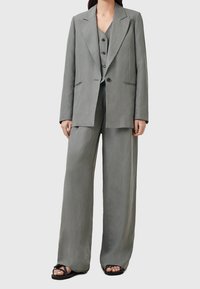 Hellgrauer Anzug mit einem taillierten Blazer mit scharfen Revers, locker sitzenden Hosen und einer Weste mit drei Knöpfen darunter. Glatte Textur.
