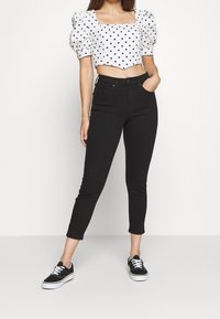 Svarta tight jeans med hög midja, kombinerat med en vit topp med prickar som är kort i modellen, med puffärmar och fyrkantig halsringning.