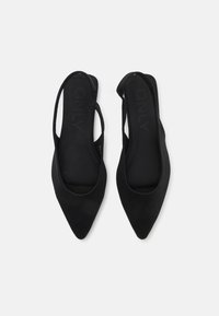 Melni slingback apavi ar norādītu purngalu un gludu auduma tekstūru. Iekļauj sānos izgriezumu dizainu papildu ventilācijai.